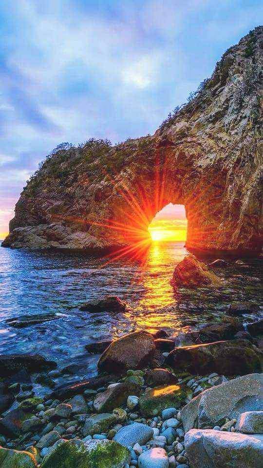 A sunset is seen through the arch of an ocean cave.